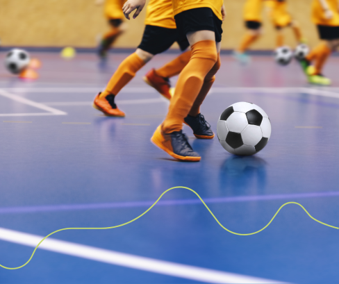 benen van voetballers met een bal in een sporthal met blauwe vloer